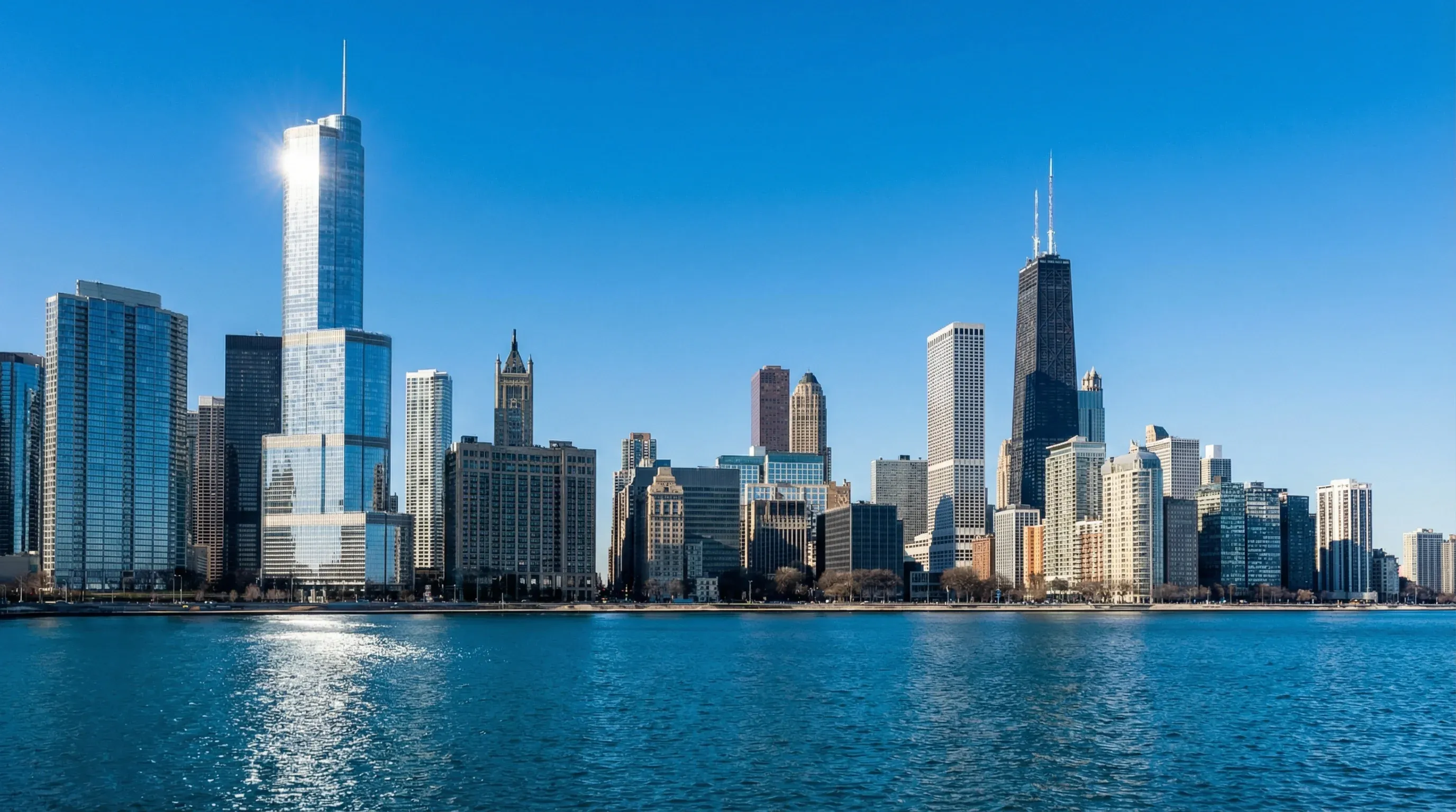 The city skyline of Chicago with high-rise buildings reflecting in the blue water of Lake Michigan.