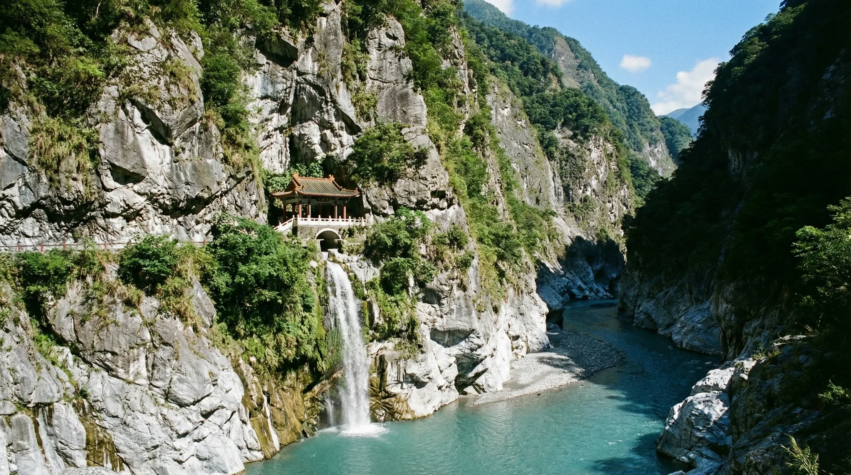 A traditional pavilion built into a steep marble cliff with a waterfall flowing into a river in Taroko Gorge.