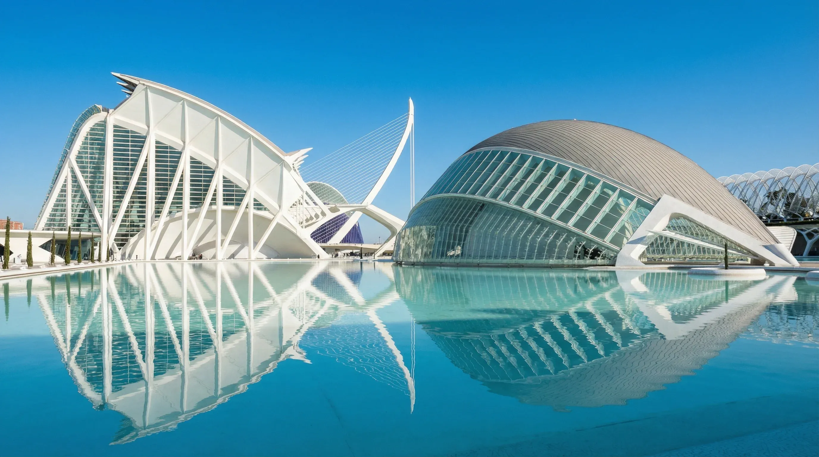 The futuristic white buildings of the City of Arts and Sciences in Valencia reflected in still blue water.