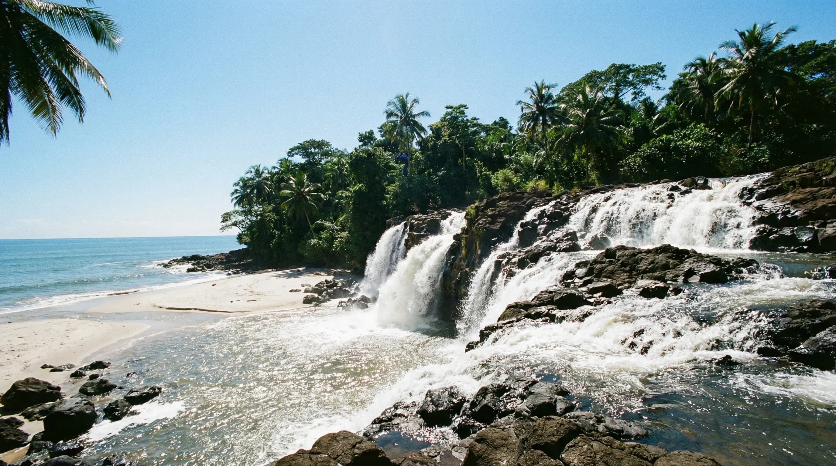 The Lobé Waterfalls flowing over rocks and onto a sandy beach directly into the Atlantic Ocean near Kribi.